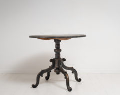 Large black tilt-top table with a large center table top and pedestal base with 4 ornate legs. The shape of the legs is unusual