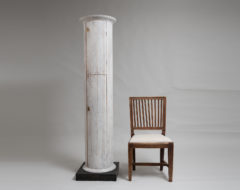 Round white column cabinet in the shape of a pillar with 2 doors and interior shelves. The cabinet is pine and revolves on the black plinth